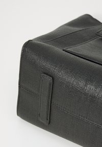 Black textured bag with a rectangular shape, featuring a stitched detail and a small handle on one side for easy carrying.