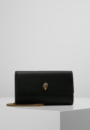 Musta teksturoidun nahkainen clutch-laukku, jossa on kultainen käärmekuvion solki ja kultainen ketjuhihna, asetettuna valkoisen jalustan päälle yksinkertaista taustaa vasten.