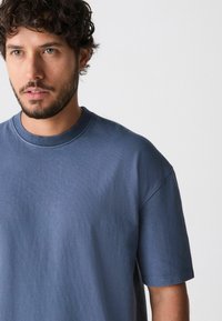 Blaues Baumwoll-T-Shirt mit rundem Ausschnitt, kurzen Ärmeln und lockerer Passform. Weiche Textur und minimale Nähedetails sind sichtbar.