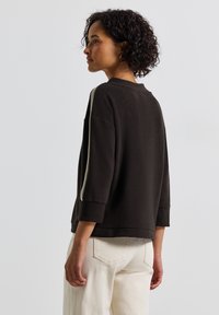 Brauner Pullover mit 3/4-Ärmeln und Rundhalsausschnitt. Mit einem kontrastierenden hellen Streifen entlang der Schulter. Weicher, strukturierten Stoff.