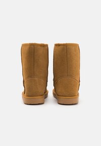 Tan suede nilkkurit, joissa on pehmeä pinta, pyöreä kärki ja vahvistetut saumat. Pohja on litteä ja valmistettu kumista, mikä antaa hyvän pidon.
