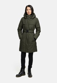 Grøn, polstret parka med bælte i taljen, stor hætte og sidelommer, båret over sort slim-fit bukser og sorte snørebåndsstøvler.