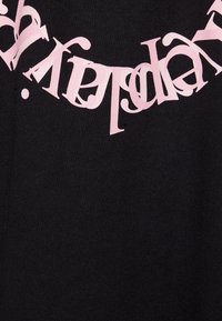 Schwarzer Stoff mit unregelmäßigem, kopfstehengem pinken Text, der über die Oberfläche verstreut ist und ein kontrastierendes Design mit variierter Typografie schafft.