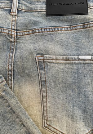 Lichtblauwe denim jeans met zichtbare vervaging, oranje stiksels en een zwart leren label op de achterkant van de taille met reliëftekst.