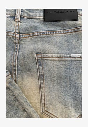Lichtblauwe denim jeans met zichtbare vervaging, oranje stiksels en een zwart leren label op de achterkant van de taille met reliëftekst.