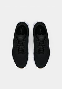 Ein Paar schwarze Tommy Hilfiger Sneaker mit weißen Sohlen, Netzstruktur und Schnürsenkeln, von oben auf einem weißen Hintergrund betrachtet.