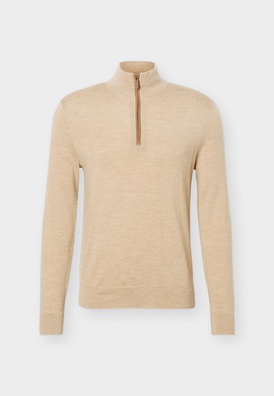 Pull beige à manches longues avec un col haut et une courte fermeture éclair frontale, présenté sur un fond clair uni.