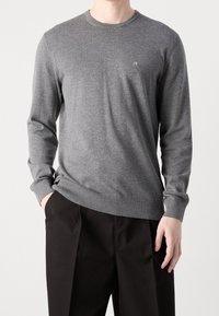 Maglione grigio a maniche lunghe realizzato in tessuto morbido, con scollo rotondo e sottile logo "ck" sul petto. Polsini e orlo a coste.