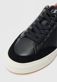 Sapatilha preta de pele com biqueira em camurça, língua acolchoada e atacadores pretos. Apresenta uma sola de borracha branca com um acabamento texturizado.