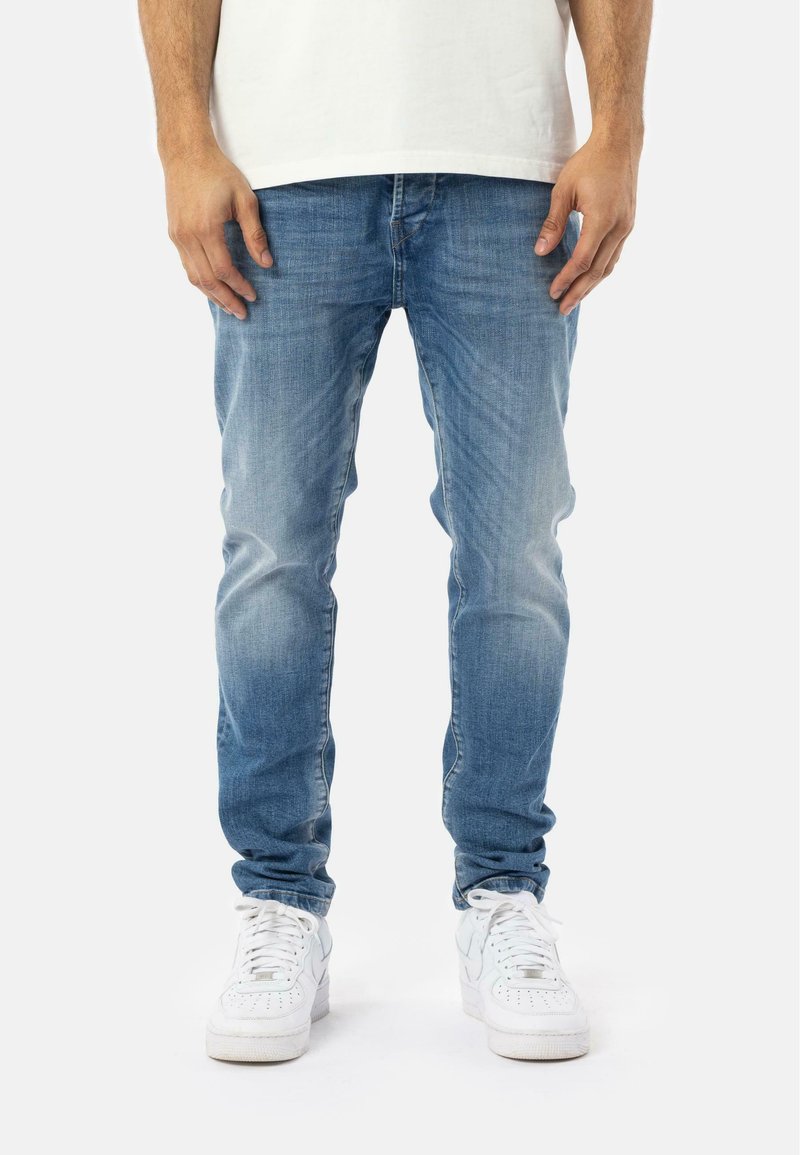 Vaqueros de denim de color azul claro con un corte slim, que presentan un lavado desvaído y un diseño clásico de cinco bolsillos. Combinados con zapatillas blancas.