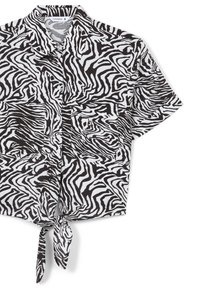 Camicia a maniche corte con stampa zebra in bianco e nero, colletto, bottoni frontali e orlo annodato in vita. Presenta due tasche sul petto.