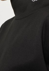Černý rolák vyrobený z hladké látky, s vysokým límcem a minimalistickým designem, na krku s malým bílým logem.