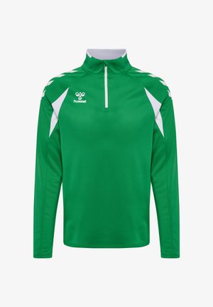 Grøn sportstrøje med lange ærmer med hvide chevronmønstre på skuldrene, kvart lynlås foran og hvidt logo på brystet.