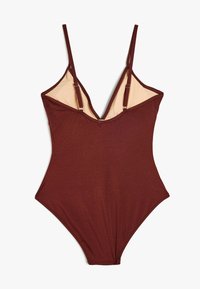 Maillot de bain une pièce bordeaux avec des bretelles réglables, un design en V et une texture lisse. L'intérieur est doublé d'une couleur beige clair.