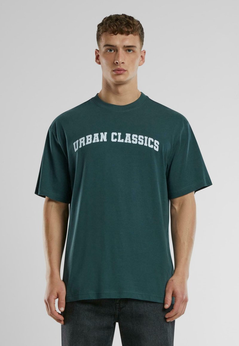 Zöld pamut póló laza szabással, kerek nyakkal és rövid ujjal. A mellkason vastag fehér betűkkel van feltüntetve az "URBAN CLASSICS" felirat.