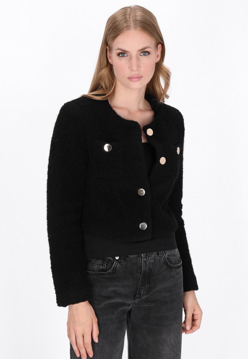 Zwart cropped jack met een fuzzy textuur, voorzien van een ronde kraag, twee voorkruiszakken en zilveren knopen voor sluiting en decoratie.