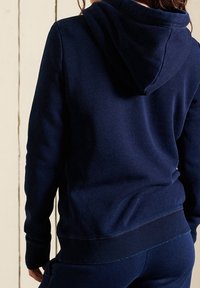 Sudadera azul marino hecha de un tejido suave, con un corte relajado, mangas largas y una capucha texturizada. Los puños y el dobladillo acanalados aportan estructura.