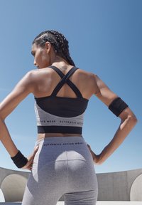 Schwarzes und graues Sportbekleidungsset mit einem Sport-BH mit überkreuzten Trägern und hochgeschnittenen Leggings mit Logo-Akzenten. Glatte Stoffoberfläche.