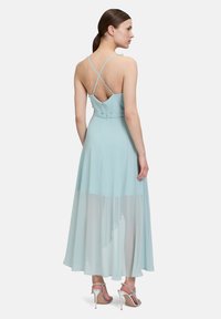 Jasnoniebieska, bezrękawnikowa sukienka z dopasowaną górą, skrzyżowanymi ramiączkami z tyłu i zwiewną spódnicą z przezroczystą nakładką, w zestawie z srebrnymi szpilkami.