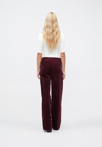Pantaloni largi din catifea côtelată de culoare burgundy, cu buzunare în spate, asortați cu un top alb mulat, cu dantelă la mâneci.