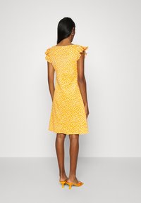 Żółta sukienka w białe kropki, krótki falbaniasty rękaw i rozkloszowany dół. Dobrana z pomarańczowymi, wsuwanimi na stopy obcasami. Gładka faktura tkaniny.