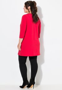 Rode tuniek met driekwart mouwen, gecombineerd met zwarte leggings en zwarte enkellaarsjes met een hak. Soepele stof, eenvoudig ontwerp.