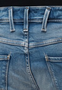 Πίσω όψη μπλε τζιν παντελονιού με θηλιές ζώνης, ζώνη μέσης, κεντρική ραφή και δύο πίσω τσέπες με εμφανείς ραφές.