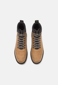 Hnědé surové hikingové boty se šněrovacím designem, černým textilním límcem a gumovou podešví, s vyztuženým švem a kovovými očky.
