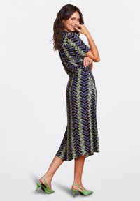 Short-sleeve dress in navy with purple and green zigzag pattern, flowy design, mid-length hem, paired with green slingback heels.