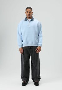 Pull polaire bleu clair avec un col zippé et un col en denim, associé à un jean noir ample et des chaussures noires avec des lacets roses.