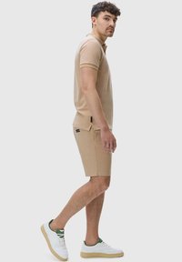 Beige polo shirt with short sleeves and a collar, paired with matching beige shorts. White sneakers with green accents. Simple design.