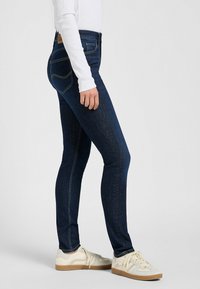 Smala mörkblå jeans i denim, med medelhög midja, stickade detaljer och två bakfickor. Kombinationen kompletteras med vita sneakers.