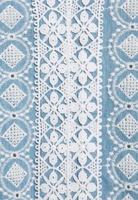 Motifs de dentelle floraux et géométriques blancs sur fond de tissu bleu en bandes verticales avec des formes circulaires et en diamant complexes.