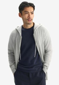 Ljusgrå zip-up hoodie med dragsko, lager på en mörk marinblå tröja, med ribbade manschetter och avslappnad passform.