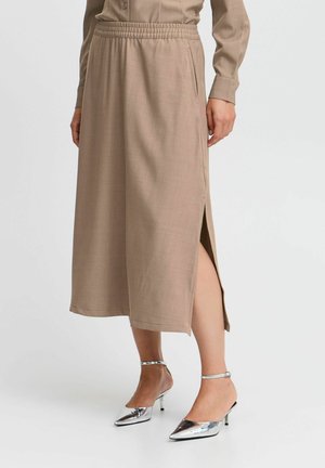 Jupe beige, longueur genou, avec une taille élastique et une fente sur le côté, fabriquée à partir d'un tissu texturé. Associée à des chaussures à talons hauts en argent brillant.