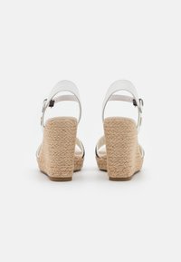 Sandali wedge in pelle bianca con tacco in juta intrecciata, dotati di una cinturini regolabile alla caviglia e una texture liscia. La vista posteriore mostra l'altezza del tacco.