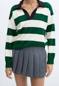 Maglione a righe verde e bianco con colletto nero, abbinato a una gonna grigia a pieghe. Il maglione ha maniche lunghe e una vestibilità rilassata.
