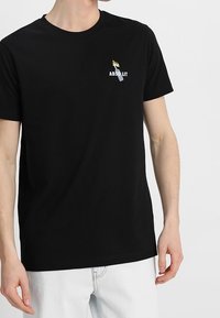 Černé bavlněné tričko s kulatým výstřihem. Má malou grafiku s textem "ABSOLIT" a designem plamenů, umístěnou na levé oblasti hrudníku.