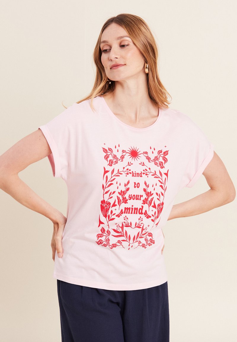 Lichtroze katoenen T-shirt met een ontspannen pasvorm, met rode bloemenprints en de tekst "vriendelijk voor je geest" centraal op de voorkant.