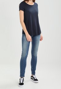 Námořnické modré tričko s krátkým rukávem spárované se světlými modrými skinny džíny, doplněné černobílými teniskami na tkaničky.