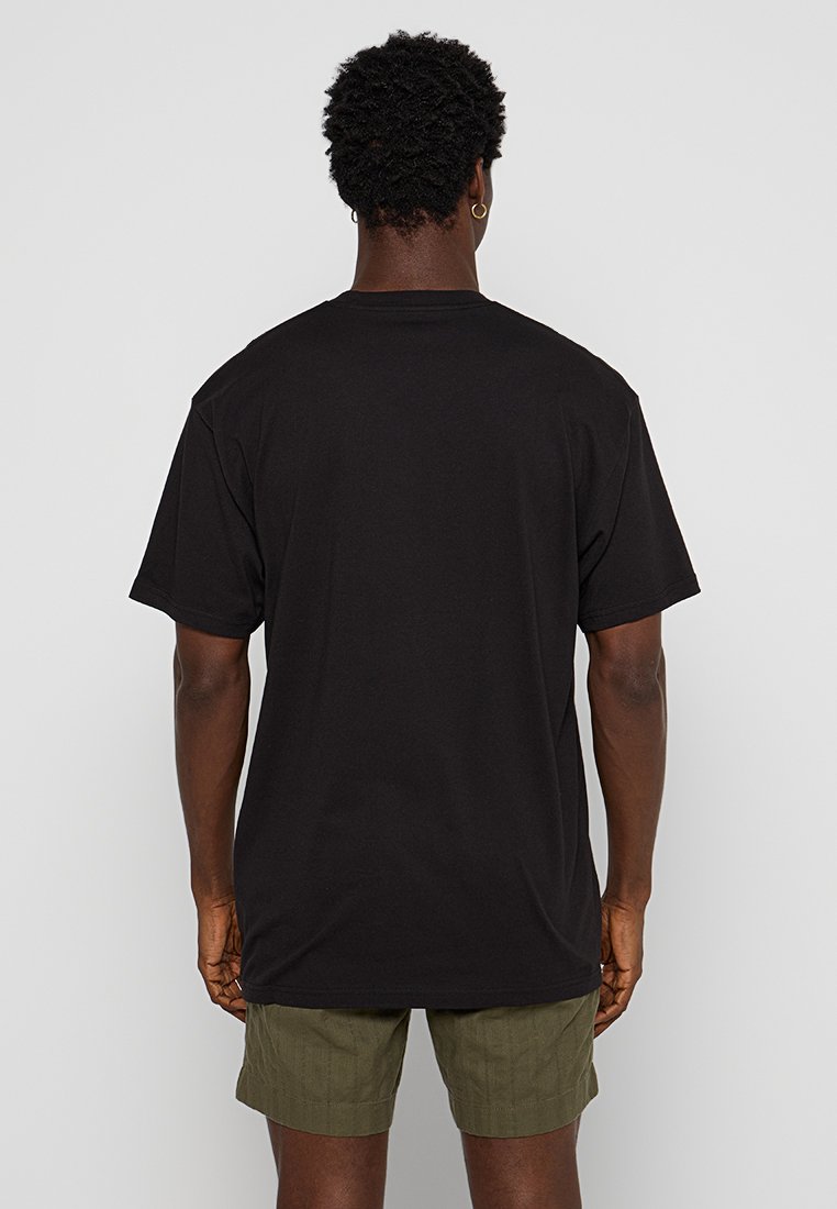 Camiseta de algodón negra de manga corta, de corte relajado y cuello redondo, vista desde la parte de atrás, combinada con pantalones cortos verde oliva.