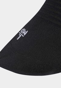 Calcetín negro con una textura suave, que presenta un ajuste ceñido, parte superior acanalada y un logo de la marca en blanco cerca del dedo del pie.