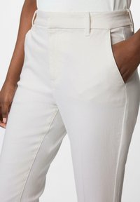 Jasno beżowe dopasowane spodnie o gładkiej fakturze, z bocznymi kieszeniami i prostym krojem. Wzdłuż szwów znajdują się subtelne detale haftu.