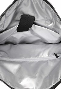 Intérieur d'un sac noir avec un revêtement argenté lisse et brillant, comprenant une poche zippée et une languette en tissu pour sécuriser le contenu.