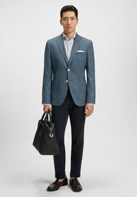 Texturerad blå kavaj med en vit skjorta, mörka byxor och bruna skor. Håller en svart läderväska. Skräddarsydd passform, med en knappstängning.