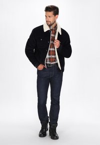 Marineblå corduroy-jakke med en cremefarvet faux fur-krave, parret med en rød og sort ternet skjorte, mørke jeans og sorte ankelstøvler.
