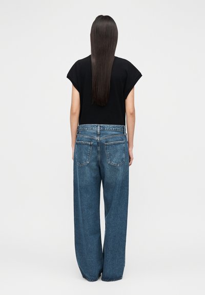 Schwarzes kurzärmeliges Oberteil kombiniert mit locker sitzenden, hoch taillierten blauen Jeans aus Denim, die Gesäßtaschen und eine leicht ausgewaschene Textur aufweisen.