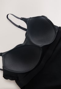 Soutien-gorge rembourré noir avec bretelles réglables, texture lisse et design sans coutures. Caractérisé par une forme de bonnet incurvée et sans éléments métalliques visibles.