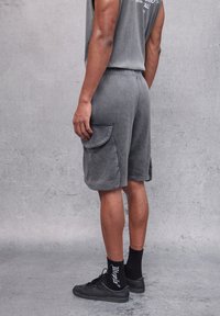 Pantaloni corti grigi fino al ginocchio realizzati in un tessuto morbido, con una grande tasca laterale e una vita elastica. Abbinati a calze scure e sneakers.