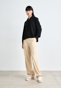 Black hooded sweatshirt with a relaxed fit, paired with beige wide-leg trousers. White sneakers with cream and beige accents.